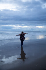 Woman pirouettes gracefully on the beach after sunset. Light still showing from between clouds. Reflection on sand. © ecummings00