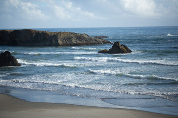 Fototapeta na wymiar Rolling waves crashing in past ridges of rock on an Oregon beach against a white cloudy sky
