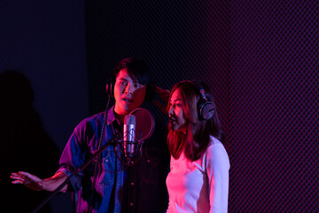 Portrait of asian young woman and man, artist singing into a microphone while recording a song in a...