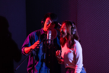 Portrait of asian young woman and man, artist singing into a microphone while recording a song in a...