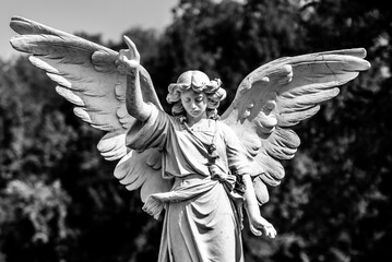Angel statue standing above a burial mound with wings spread.