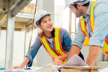 Young Asian engineers and caucasian engineer colleagues at site inspector and discuss together using notebook computer and paper blueprint at building construction site.home renovation ideas concept