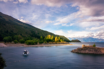 Sunset panorama at the southern end of Lake Hawea with a beautiful patch of backlit trees in the background and a small boat in shade in the foreground - Otago Region, New Zealand, Southern Alps.