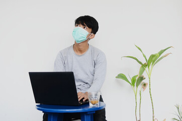 Asian young man wearing a mask sitting in front of a laptop dizzy with his job