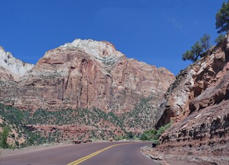 Impressive high red cliffs and layered rock formations border paved roads at Zion National Park, Utah, USA.