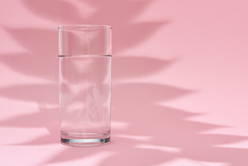 Glass of water and leaf shadow on a pink background