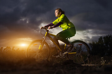 Naklejka premium Sport woman bicycling against dramatic sky background