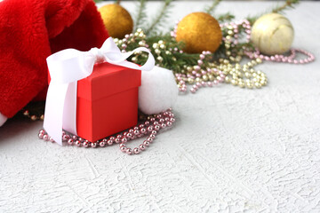 A New Year's gift tied with a white bow stands against the background of bright balls and beads. Selective focus. Concept for Christmas and New Year holidays.