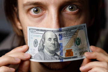 Man covers his mouth with a $100 bill