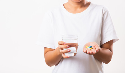 Closeup young Asian woman hold pill drugs in hand ready take medicines with a glass of water, studio shot isolated on white background, Healthcare and medical pharmacy concept