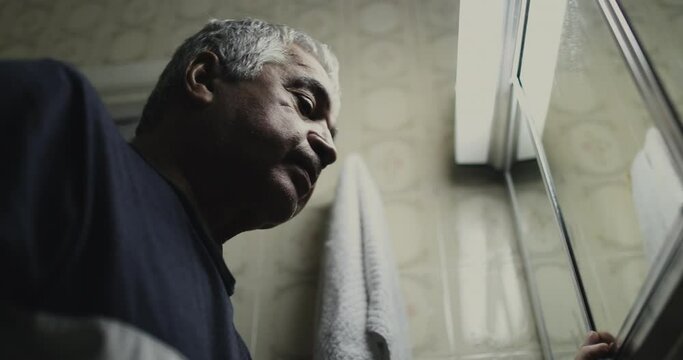 Senior in crisis in front of bathroom mirror, despair concept