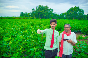 young indian handsome agronomist and farmer analyzing with test tube and tablet in field