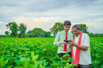 Young indian agronomist Discussing with farmer and showing some information in tablet