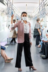 Asian business woman travelling on train in city wearing mask and pink blazer
