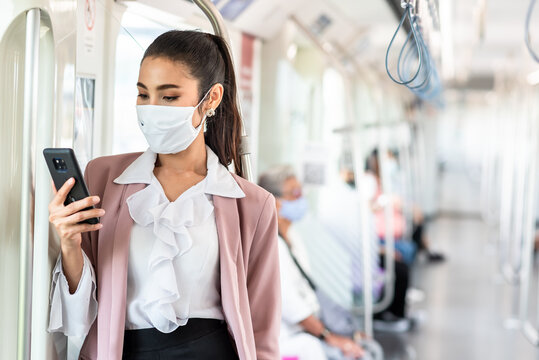 Asian Business Woman Travelling On Train In City Wearing Mask And Pink Blazer Use Smartphone