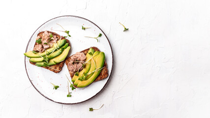 Sandwiches with avocado and tuna fish, microgreen, wholemeal bread. Delicious breakfast or snack on a light background, top view. Long banner format