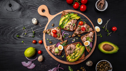 Fototapeta na wymiar Bruschetta sandwiches collection with tuna, quail egg, cherry tomatoes, avocado, microgreen and capers on a dark background, Tasty tuna sandwiches. Delicious breakfast or snack. Top view