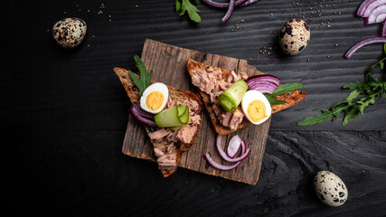 Obraz na płótnie Canvas Tuna salad sandwiches on chopping board. bruschetta toast with wholemeal bread, canned tuna fish, quail eggs and onions, cucumber