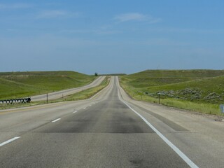 Paved road with a roadside sign with distance to Buffalo and Sheridan just out of Gillette, Wyoming.