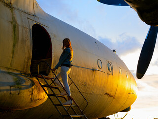 Yo ungwoman standing at plane ladder going to board, outdoors, airport. Old Soviet military airplane, sunset time. Close up of a Abandoned Historic Aircraft. Close up of propeller engine. 