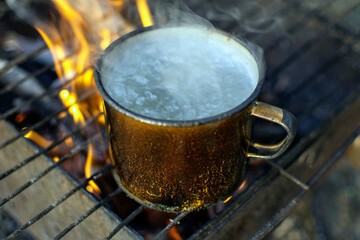 a mug of boiling water stands on a burning fire. close-up