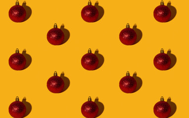 Christmas ball pattern. Orange seamless background. New Year party ornament. Winter holidays adornment. Red round shimmering glitter bauble symmetrical composition isolated on bright yellow.