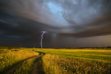 rural road in the middle of a field and a flash of lightning in the dramatic sky