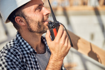 Gladsome builder holding a walkie-talkie close to his mouth