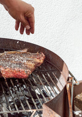 THROWING SALT OF FLAKES TO AN BEEF STEAK ON THE GRILL