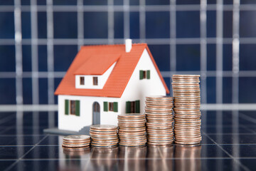 A row of increasing dollar coins and a small house model on a solar panel