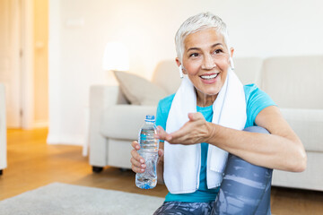 Senior woman with headphones while resting after workout. Holding a bottle of water. Athletic mature woman resting after a good workout session
