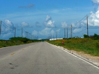 Wide road with blue skies at Galveston Island, with power poles on both sides of the road, Texas.