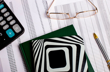 Calculator, glasses, pen and notepads on the background of reports on the desktop. Business concept