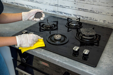 female hand in white gloves cleaning with a foam gas stove with a glass surface.