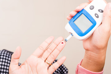 Closeup Hands woman measuring glucose test level check with blood on finger by glucometer at home she monitor and control high blood sugar diabetes and glycemic health care concept