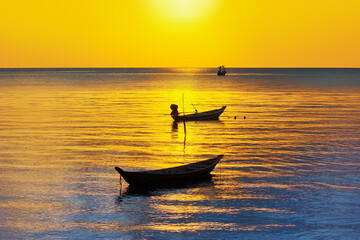 Fototapeta premium Beautiful sunset landscape, yellow sky, golden sun glow reflection on water, fisherman boats silhouette on blue sea background, ships on ocean beach, sunrise seascape, travel in Thailand, Samui island