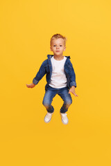 Full length portrait of excited little child boy Jumping for joy isolated on yellow background.