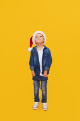 Portrait of a satisfied little child boy dressed in christmas Santa hat. laughing isolated over colored yellow background. Wow face. full-length portrait