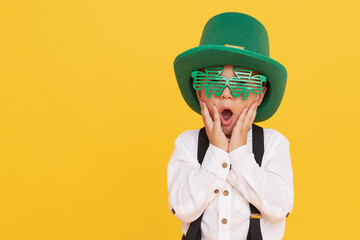 Smiling little child boy in green leprechaun hat on yellow background. St. Patrick Day celebration....