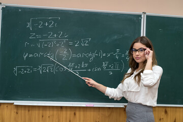 beautiful young teacher shows a pointer to the solution of math exercise in the classroom