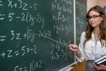 beautiful young teacher shows a pointer to the solution of math exercise in the classroom