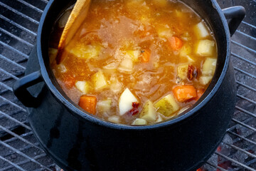 Stew cooked on fire outdoors in a cast-iron pot on a grill grid