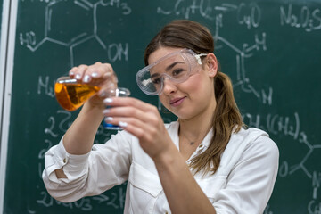Chemistry teacher holds a flask with orange liquid and conducts a scientific experiment in the classroom