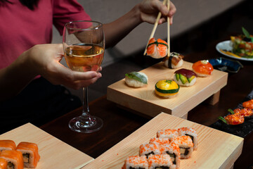 Close up shot of  woman enjoying Japanese cuisine with various side dishes, tuna uramaki, onigiri sushi set and glass of vine in restaurant