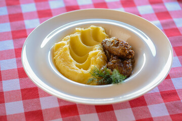 Fried fish with mashed potatoes and sauce served on a white plate over red plaid tablecloth.