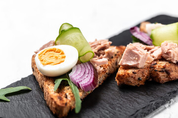 Tuna salad sandwiches on chopping board. bruschetta toast with wholemeal bread, canned tuna fish, quail eggs and onions, cucumber