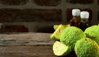 Fruit of the Maclura pomifera tree or horse apple on a wooden table. Sliced ​​Adam's apple for medical use, bottles of Maclura tincture. Close-up with copy space