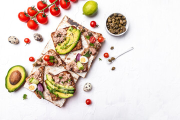Set of bruschettas with tuna, quail egg, cherry tomatoes, avocado, microgreen and capers on a light background, Toasts with tuna delicious healthy food. top view