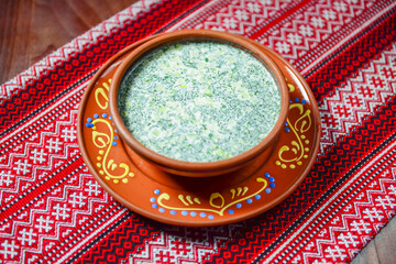 Russian and ukrainian traditional cold soup okroshka in a white bowl served over traditional Ukrainian table cloth.