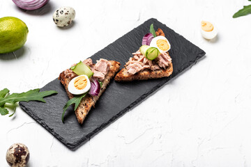 Italian bruschetta sandwiches with canned tuna, cucumber, quail eggs and onions, Toasts with tuna. Delicious breakfast or snack, top view